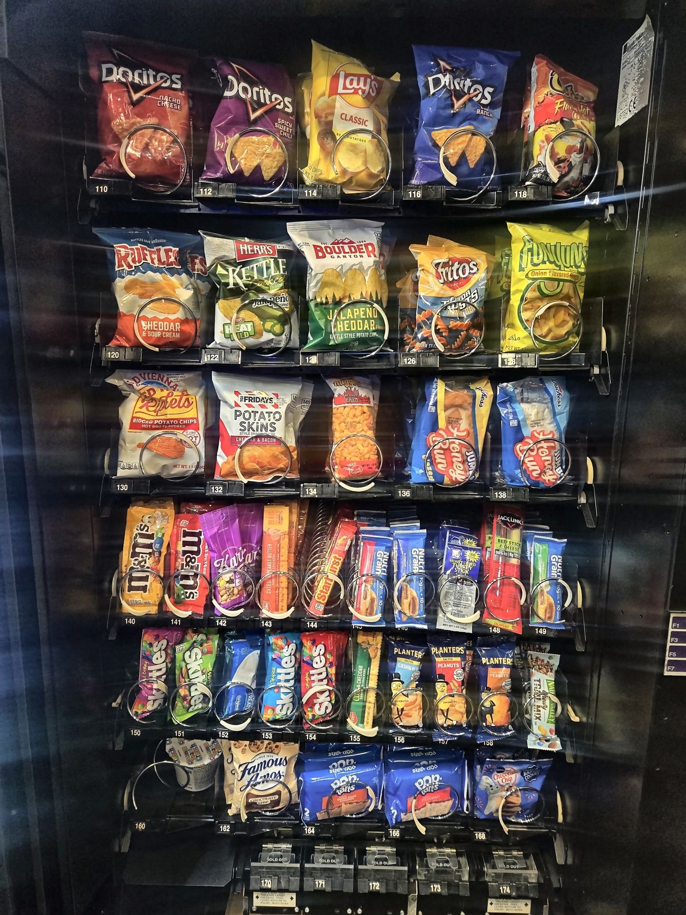 The glass front of an SKS Vending machine in a St. Charles break room, every coil loaded with chips, candy and snack bars.