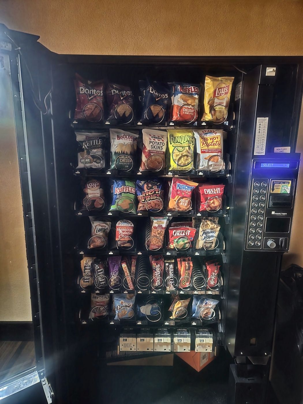 An SKS vending machine with the door swung open, every coil loaded with chips, candy and snack bars.