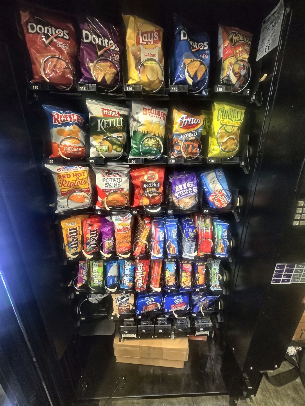 A lit vending machine in a darkened room with full rows of snacks visible through the glass.