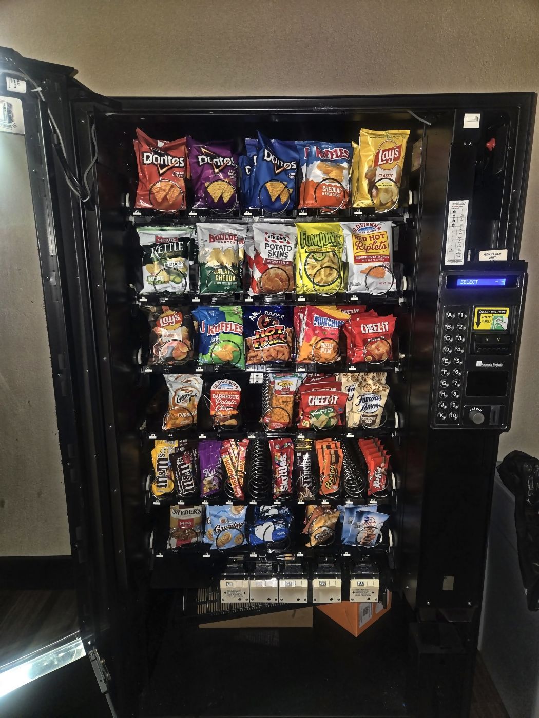 A stocked snack machine standing against the wall of a workplace break room.